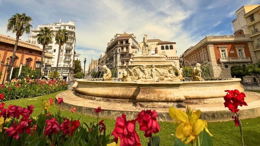 fountain in sevilla with red and yellow flowers in the foreground