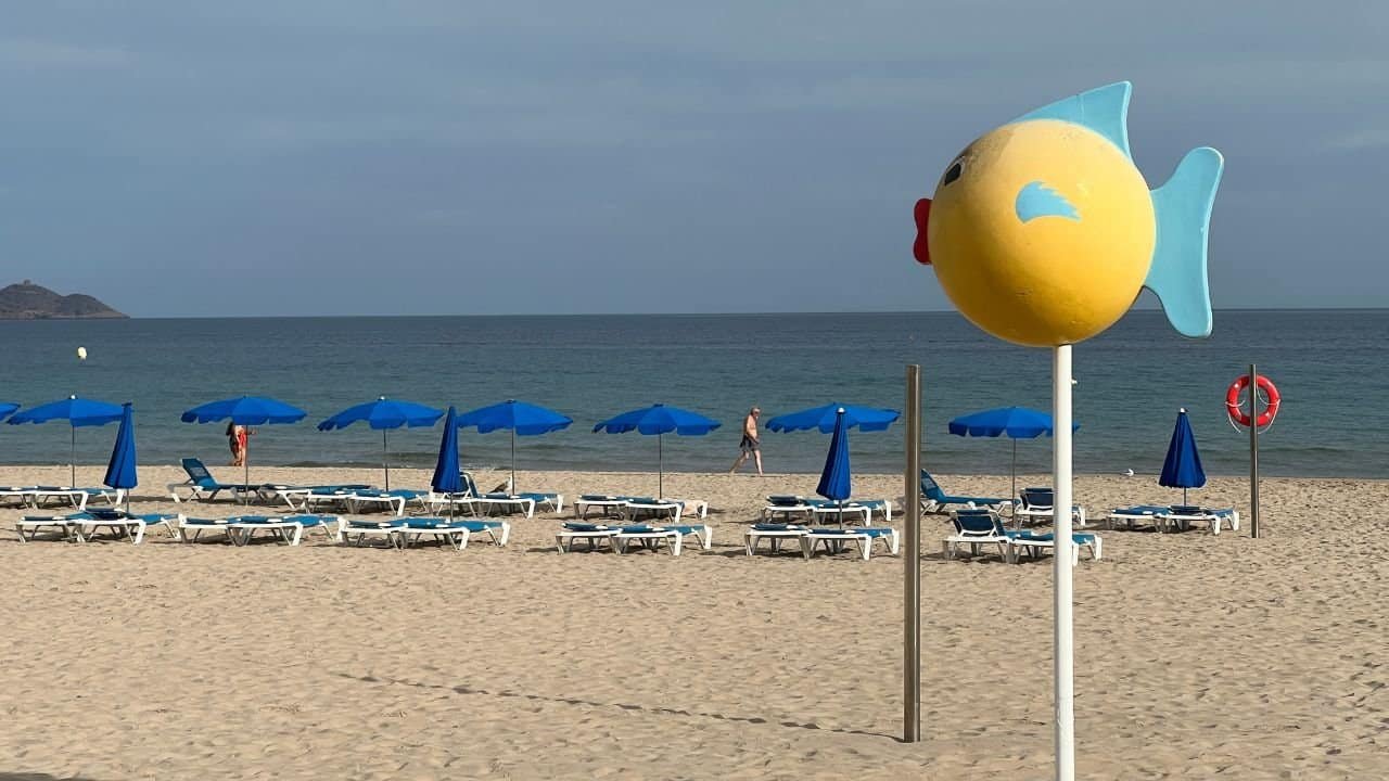 Colourful fish-shaped beach sign on sandy shoreline with beach chairs and umbrellas | Iconic guide to relaxing retirement seaside destinations in Australia.